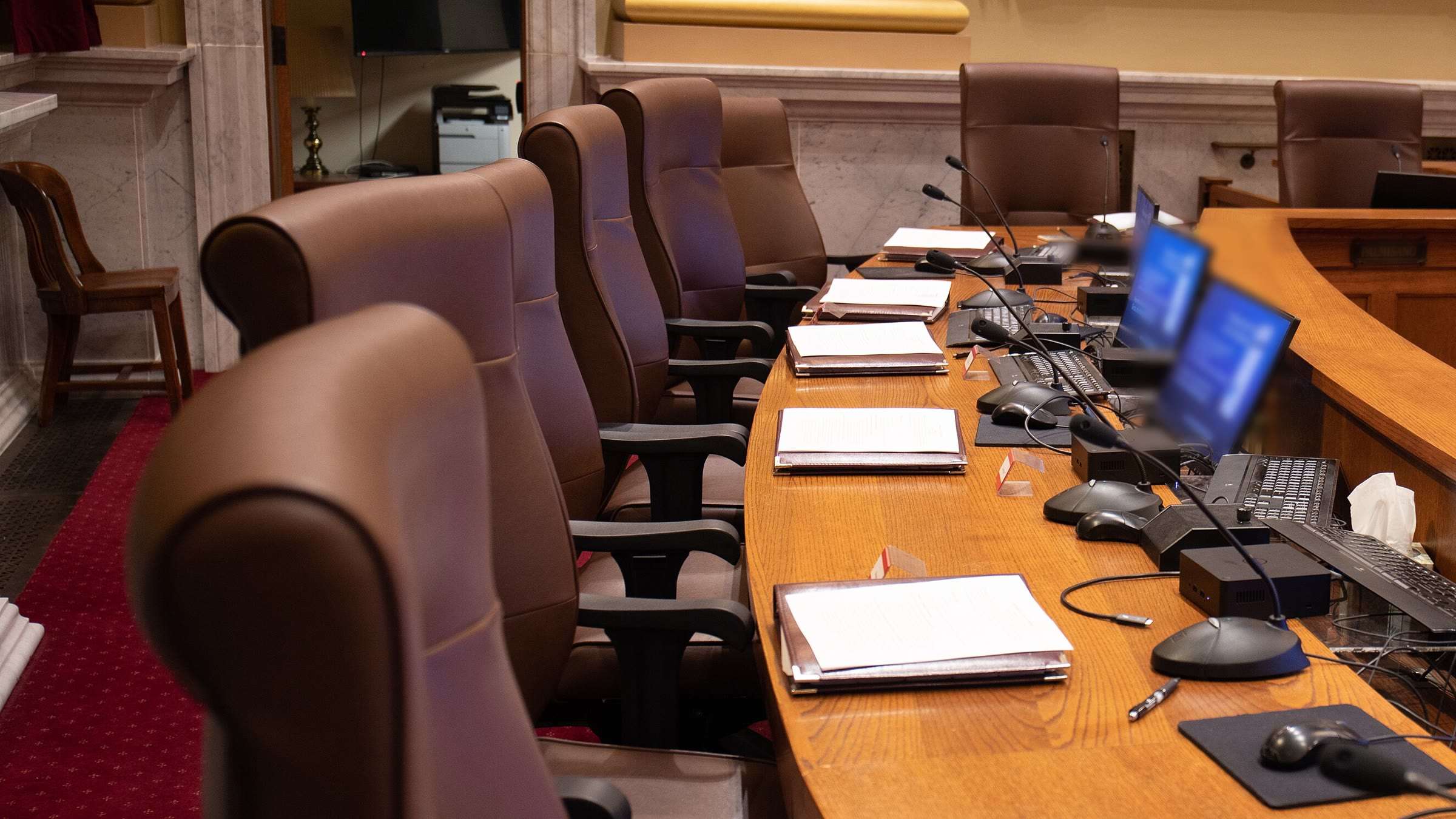 A council chamber's dais with chairs, microphones and meeting packets.